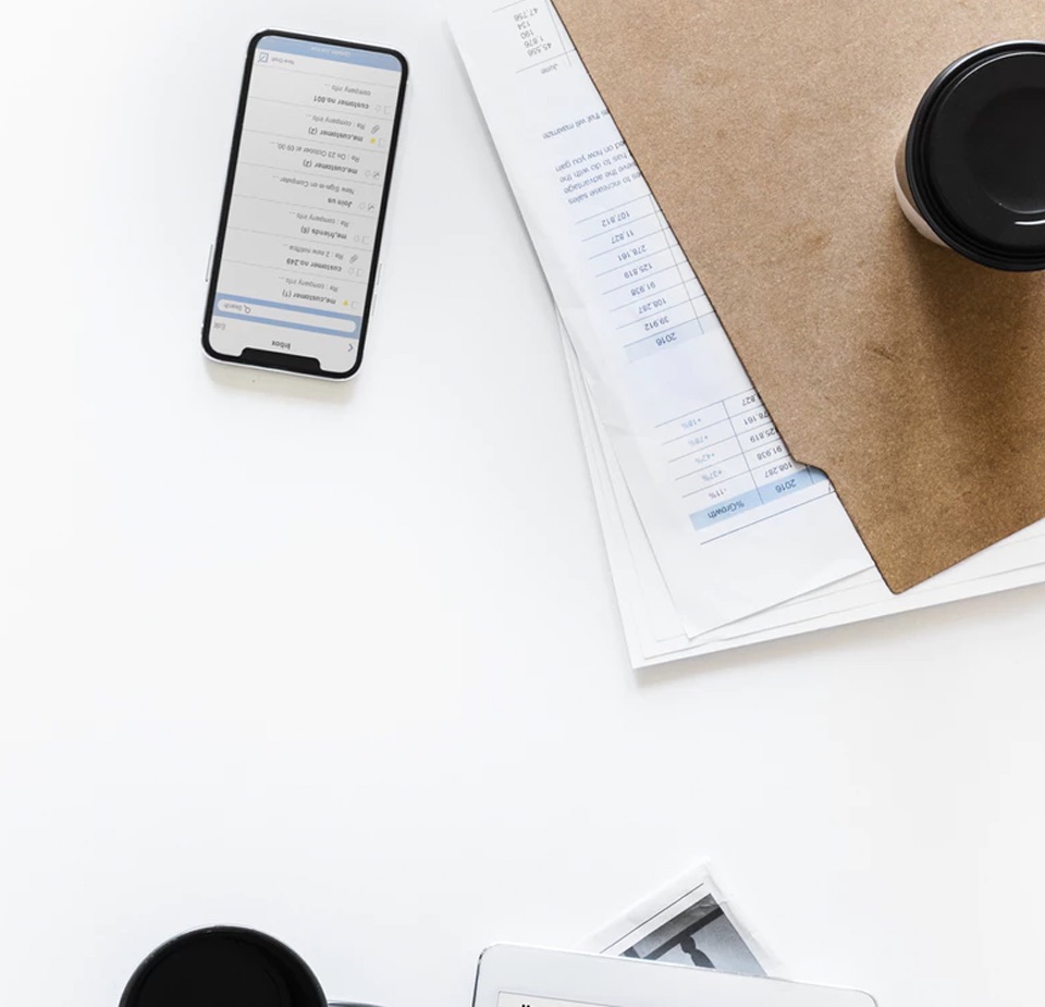 Top down view of a cell phone and coffee cup on folder with paper in it.